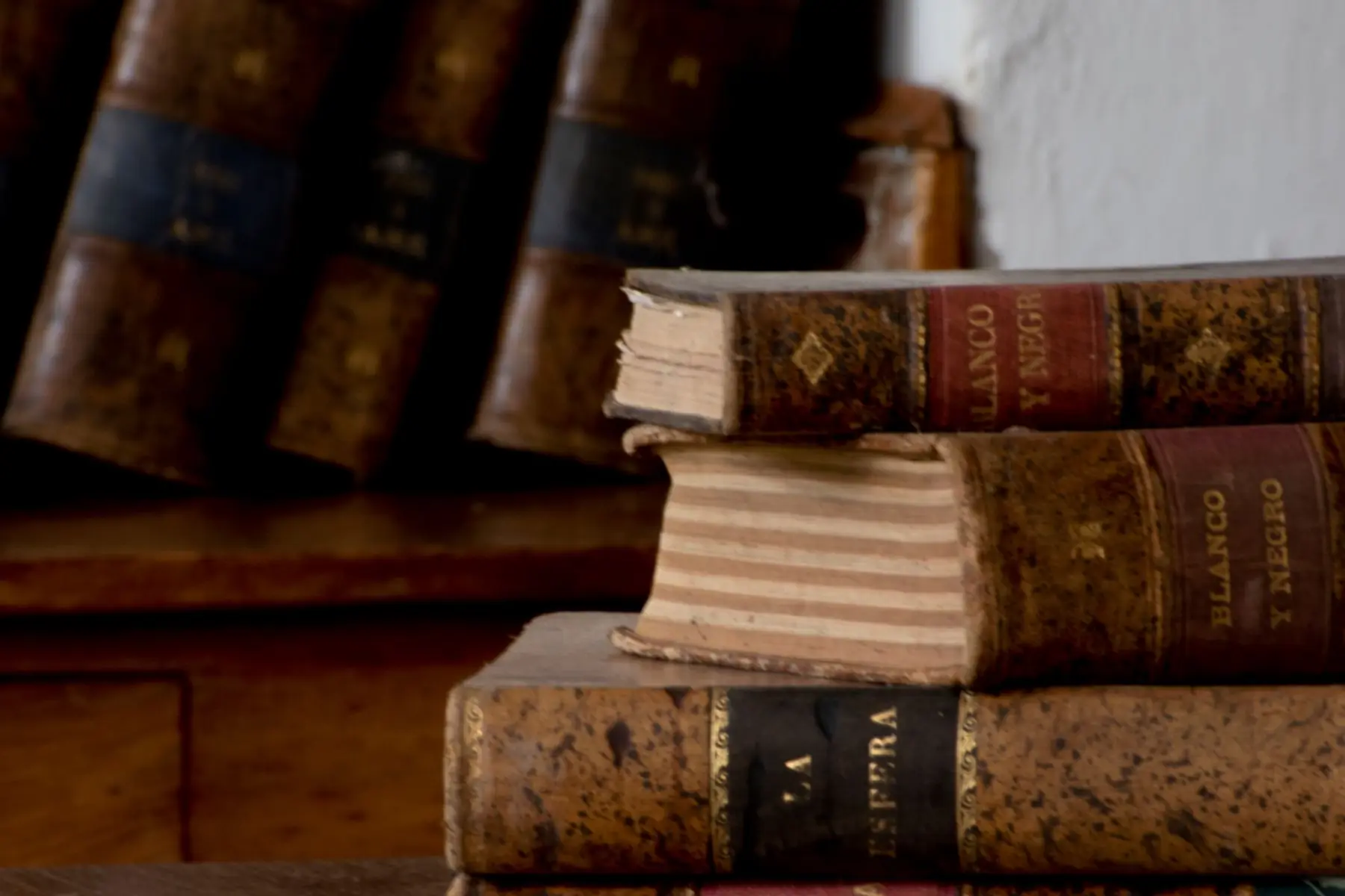 Volúmenes antiguos encuadernados en piel apilados junto a la librería del despacho